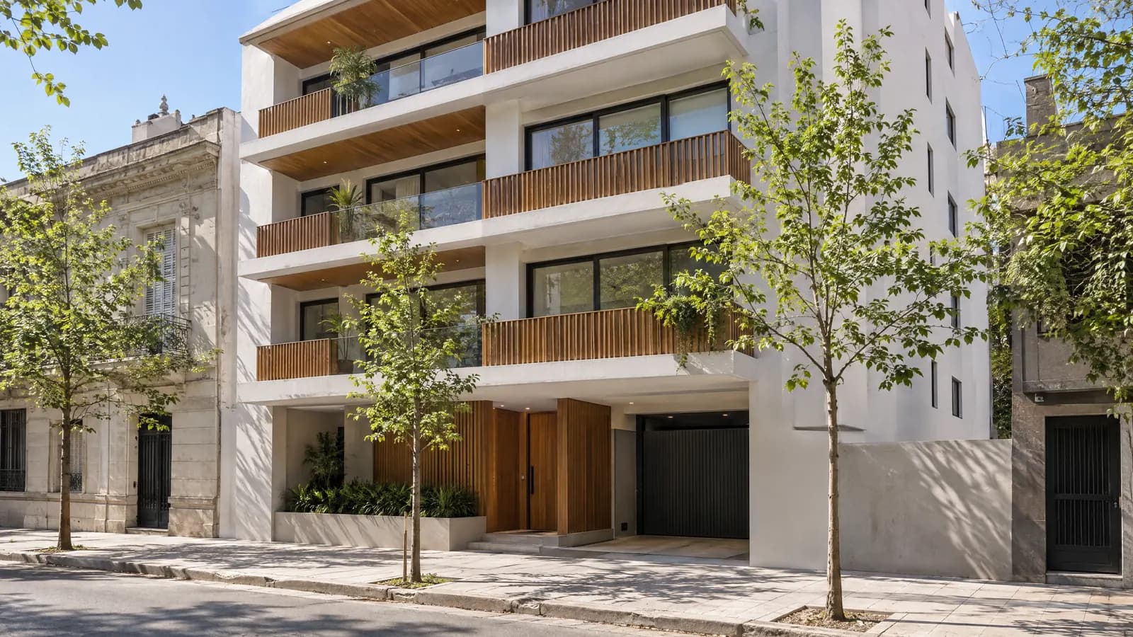 Edificio residencial recién terminado con fachada blanca y árboles jóvenes en la vereda.